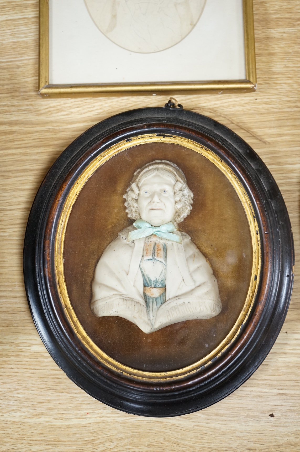 Four Regency and early Victorian portraits to include a pair of a lady and gentleman together with a carved wax bust of a lady wearing a bonnet, housed in an ebonised and gilt oval box frame, largest overall 38 x 32cm